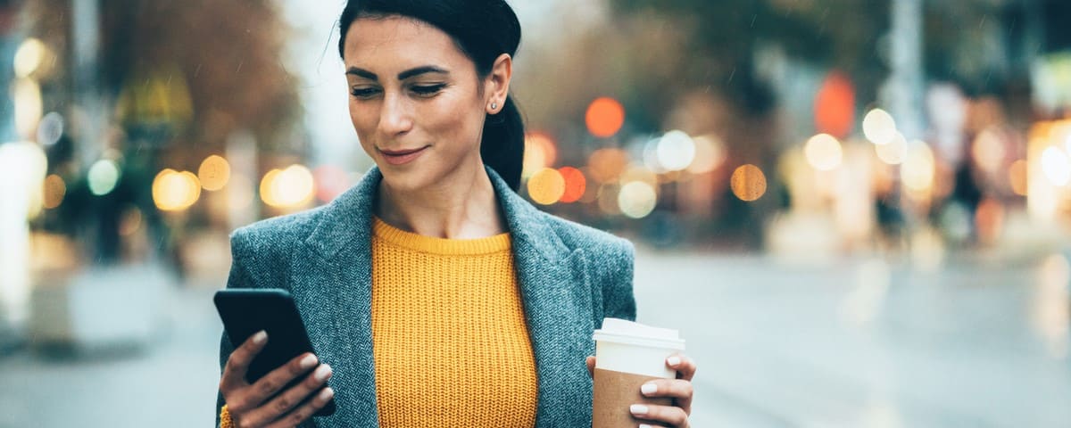 Femme heureuse tenant son téléphone et son café en pleine rue